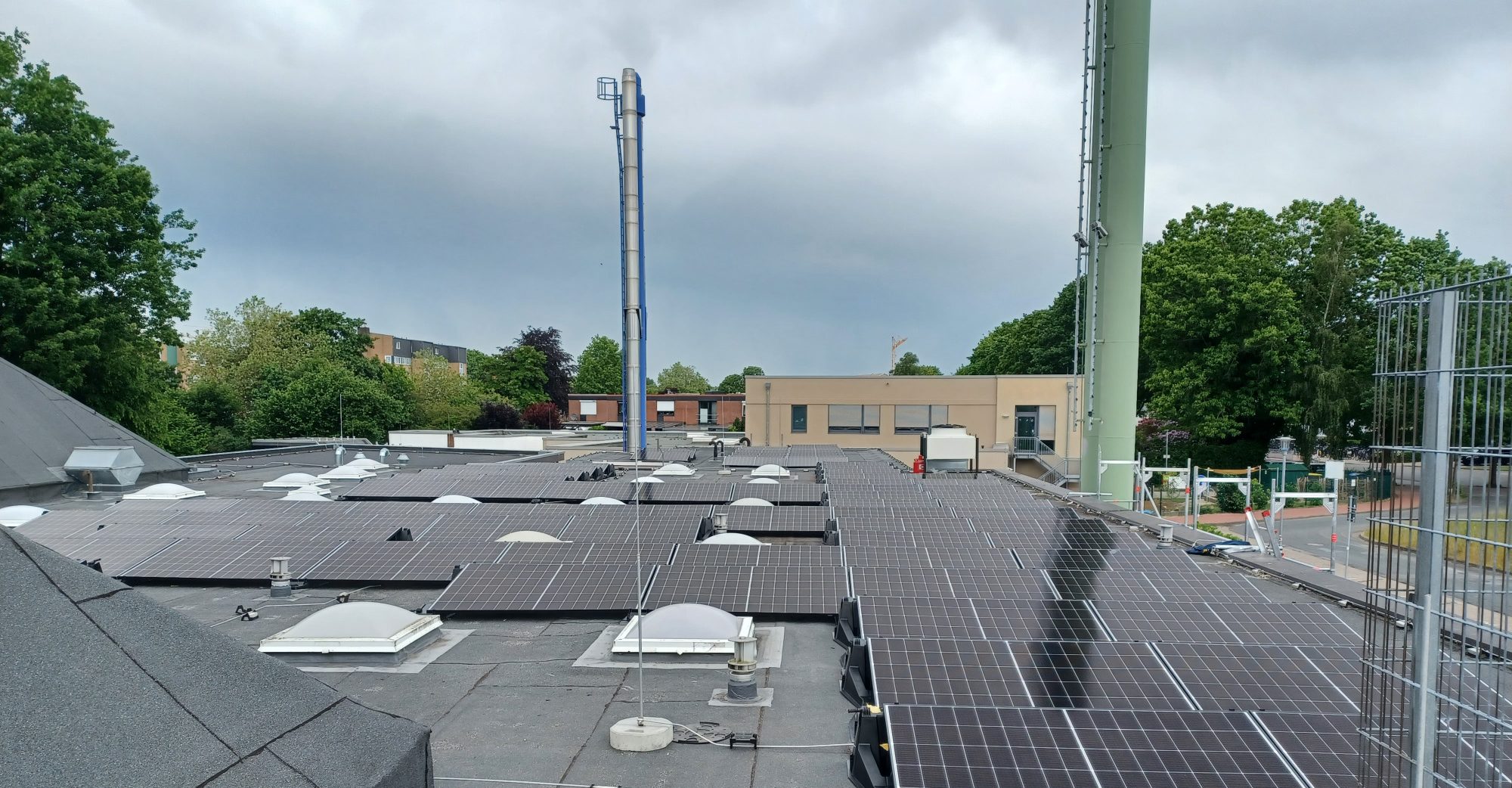 Aufbau der Anlage "Hallenbad Lilienthal" Dach mit Solarpanels und Umgebung, darunter Bäume und ein Gebäude.